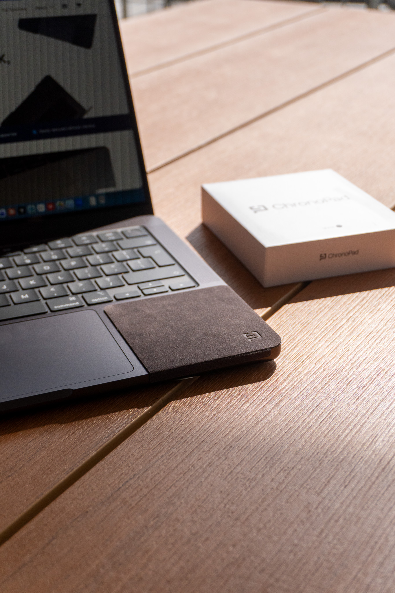 MacBook with ChronoPad applied next to the ChronoPad packaging on a desk