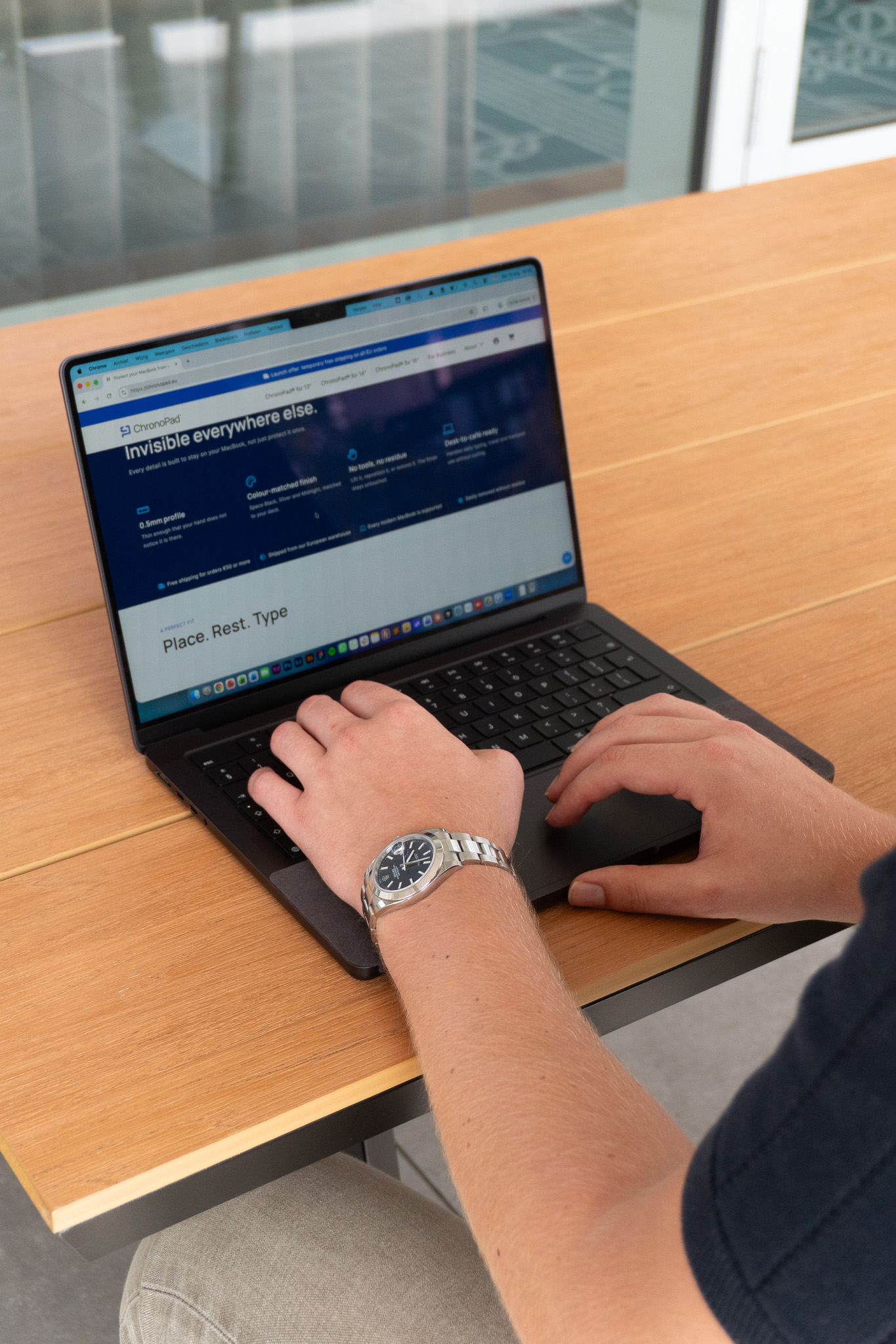Typing on a MacBook while wearing a steel watch bracelet at a desk