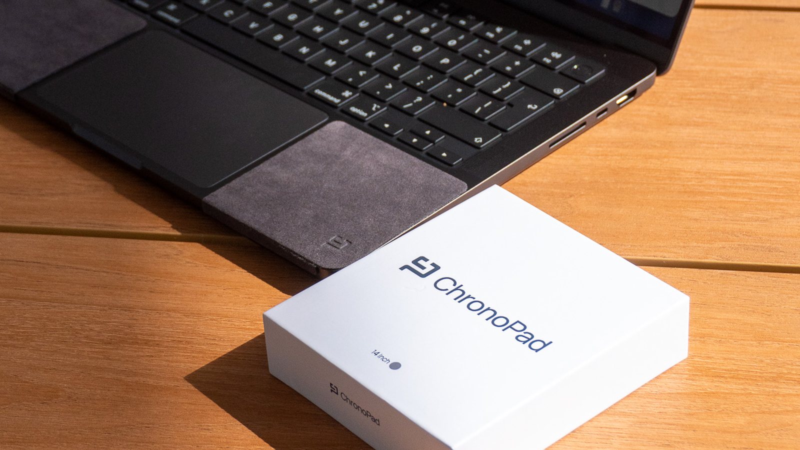 Caja de regalo de ChronoPad junto a un MacBook con pads ChronoPad en un escritorio de madera