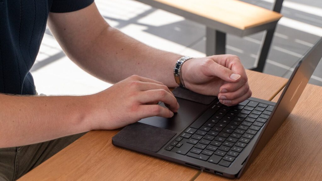MacBook sharp edges: hands typing on a MacBook Pro with a ChronoPad pad under the wrist and a steel watch bracelet