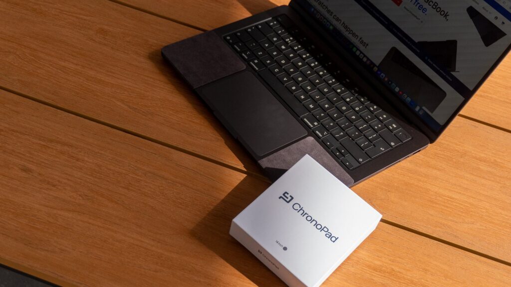 MacBook skins vs a palm rest protector: MacBook Pro with ChronoPad pads next to the ChronoPad box on a wooden desk